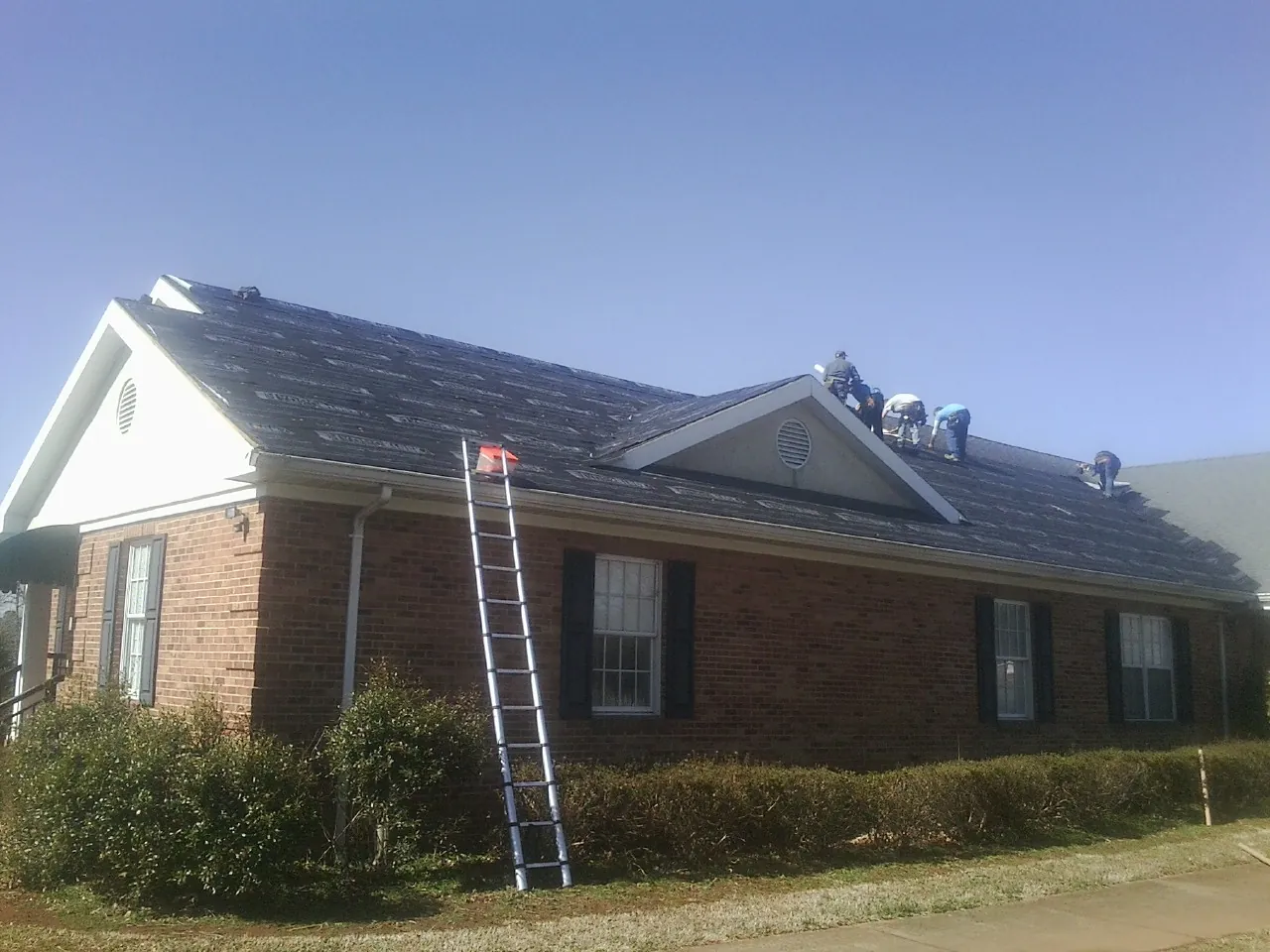 Crew tearing shingles off a brick ranch roof with a ladder set — Metal Roof Repair work by our crew in Middleburg